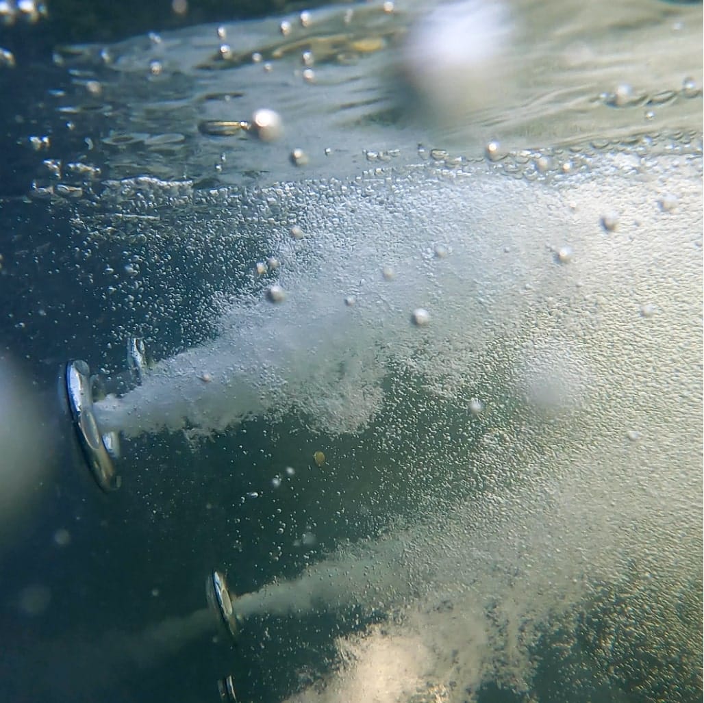 Underwater view of two metal water jets releasing streams of bubbles in clear water environment