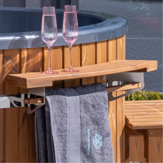 Close-up of wooden shelf attached to hot tub with two pink champagne flutes and a gray towel hanging below