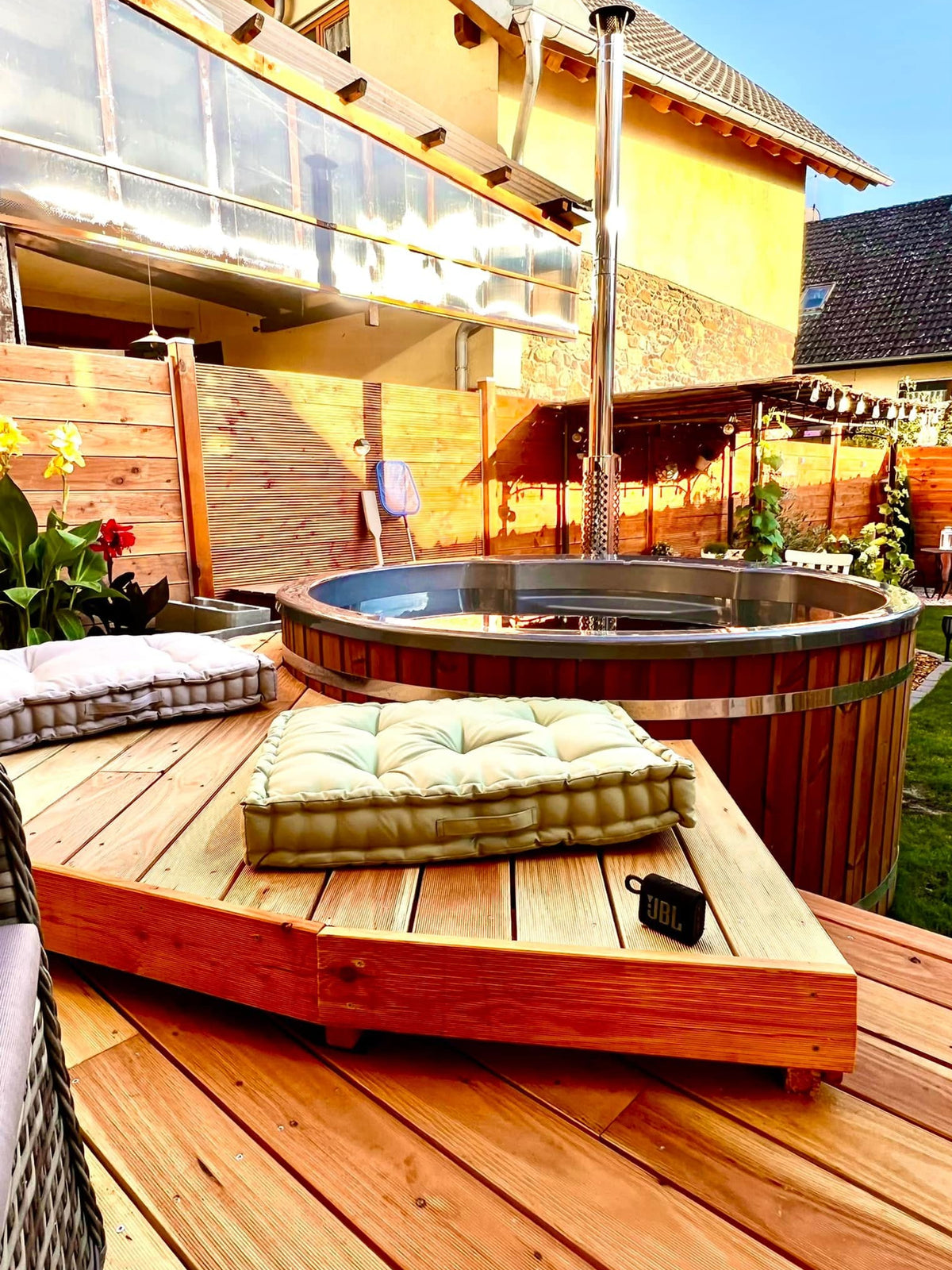 Gardenvity wood fired hot tub on raised wooden decking with cushions and modern backyard decor.