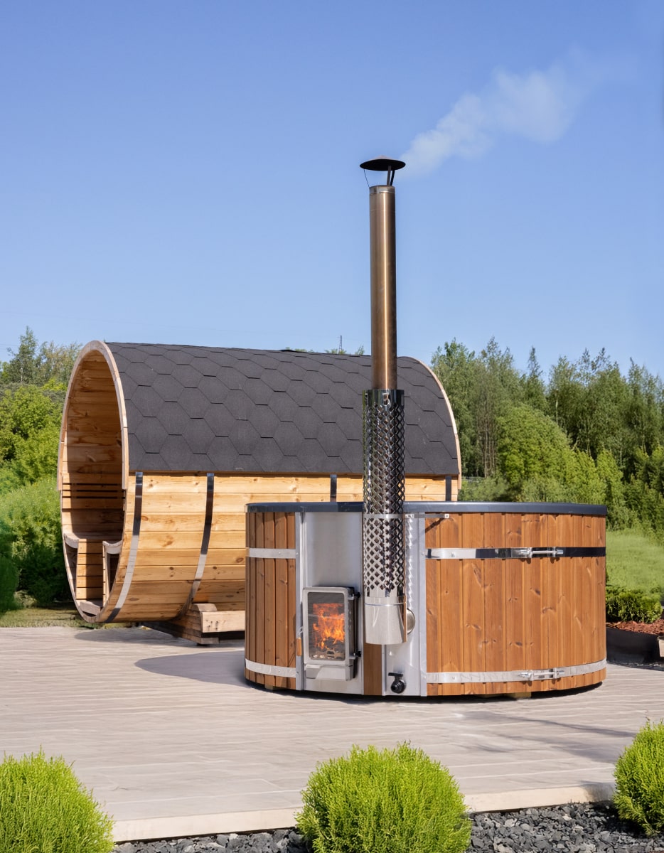 Outdoor view of wooden hot tub with external wood stove and barrel sauna in garden setting under clear sky