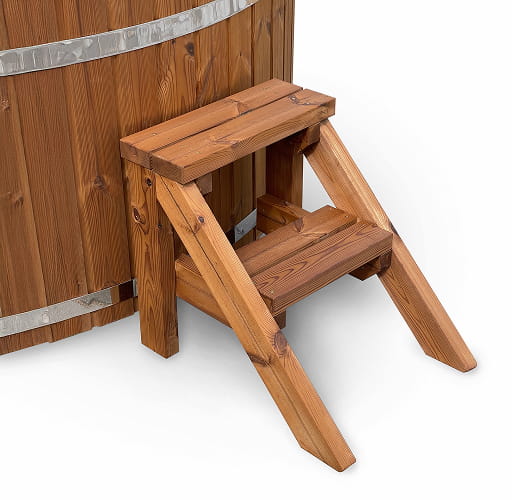 Outdoor view of wood fired hot tub with dark interior, wooden steps, towel rack, and hexagonal sauna cabin nearby